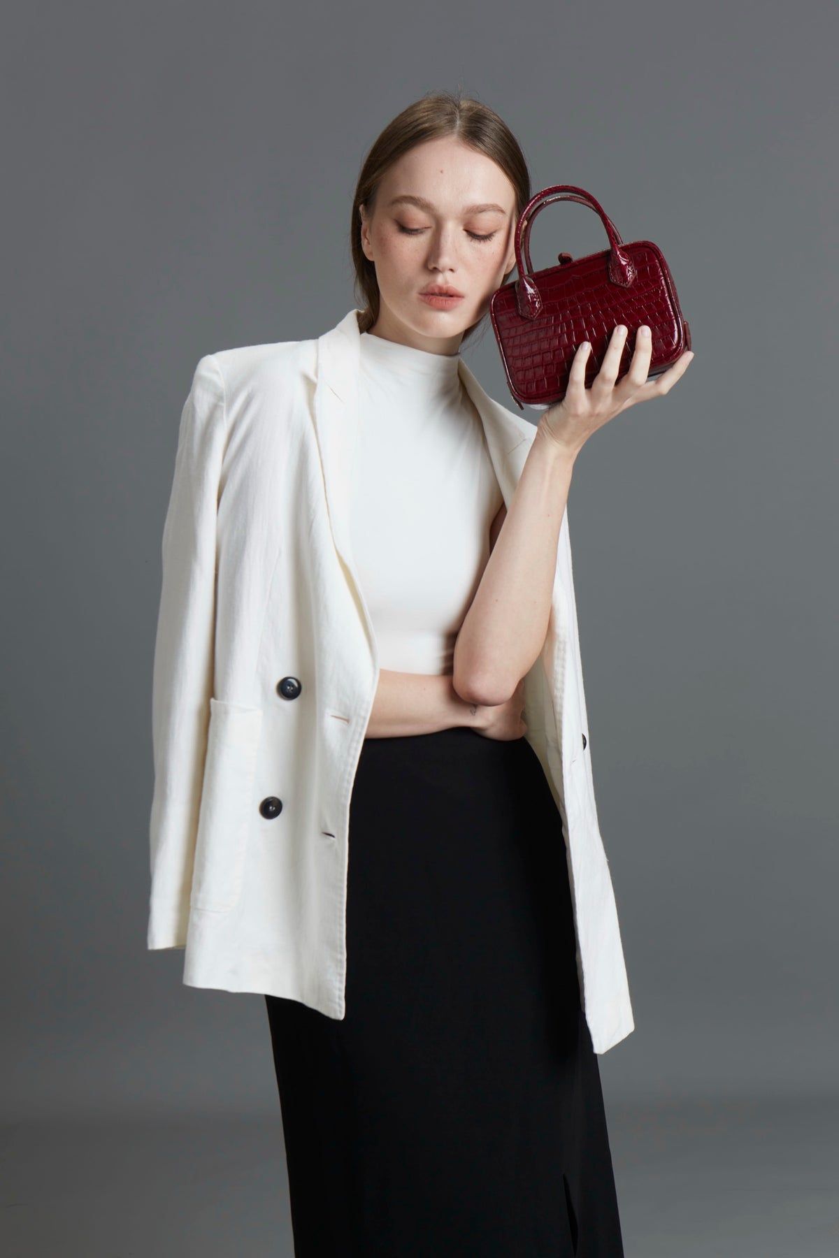 Model holding a small burgundy croc-texture Klove handbag
