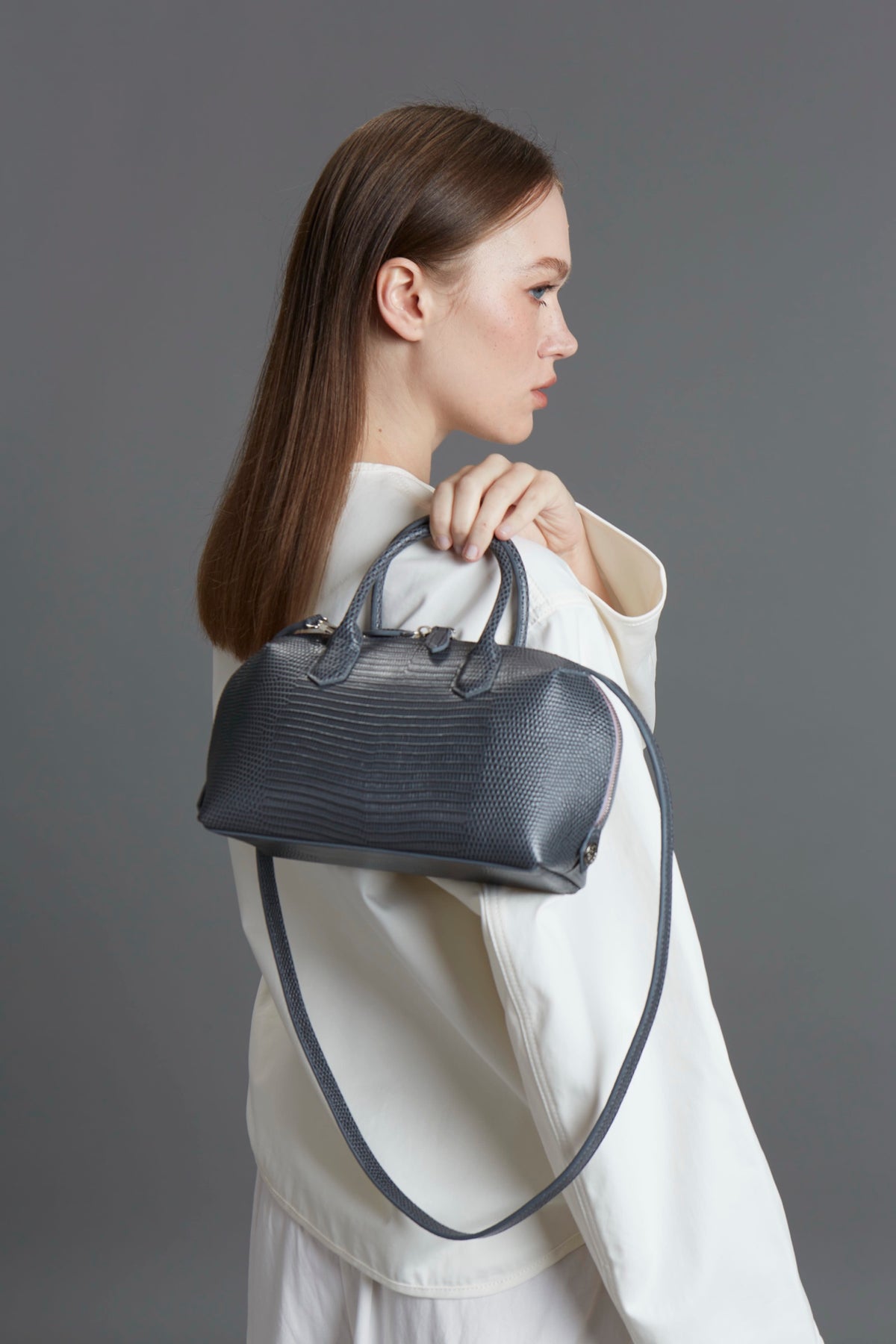 Model holding a grey lizard-texture Klove top-handle bag