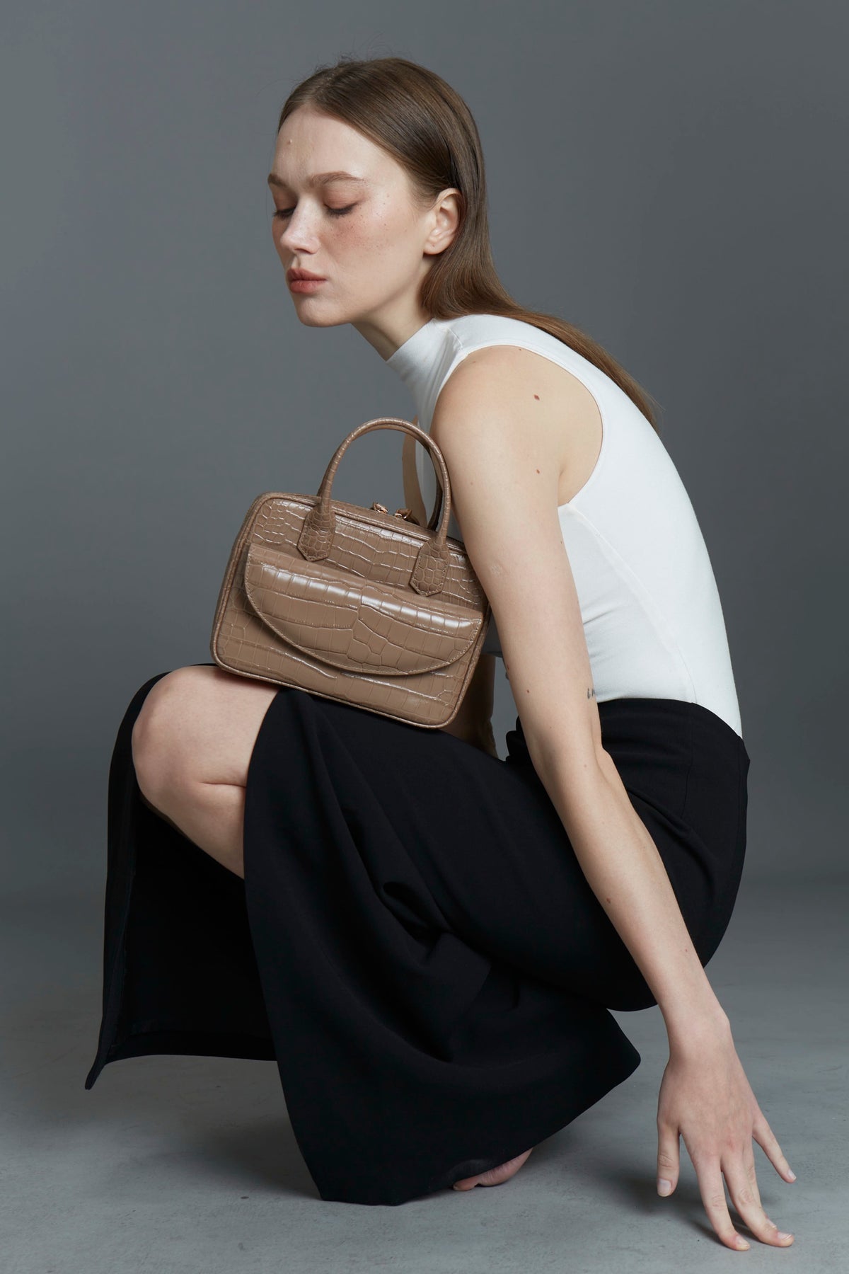 Model crouching with a taupe croc-texture Klove top-handle bag